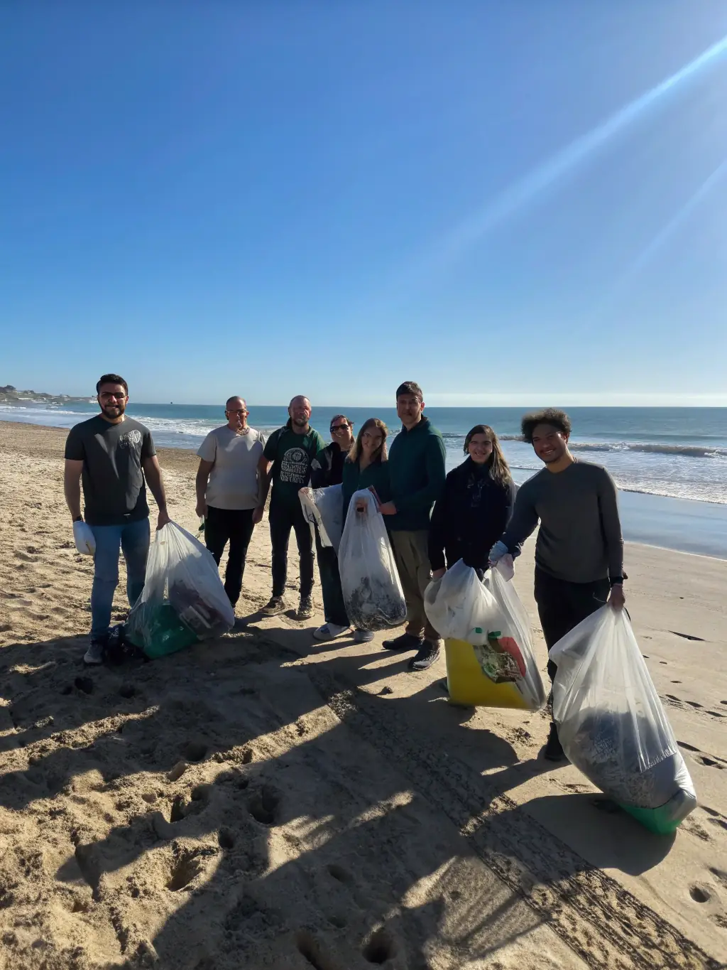 A photograph capturing volunteers cleaning up a beach in Beautiran, removing plastic waste and debris, under a clear blue sky.